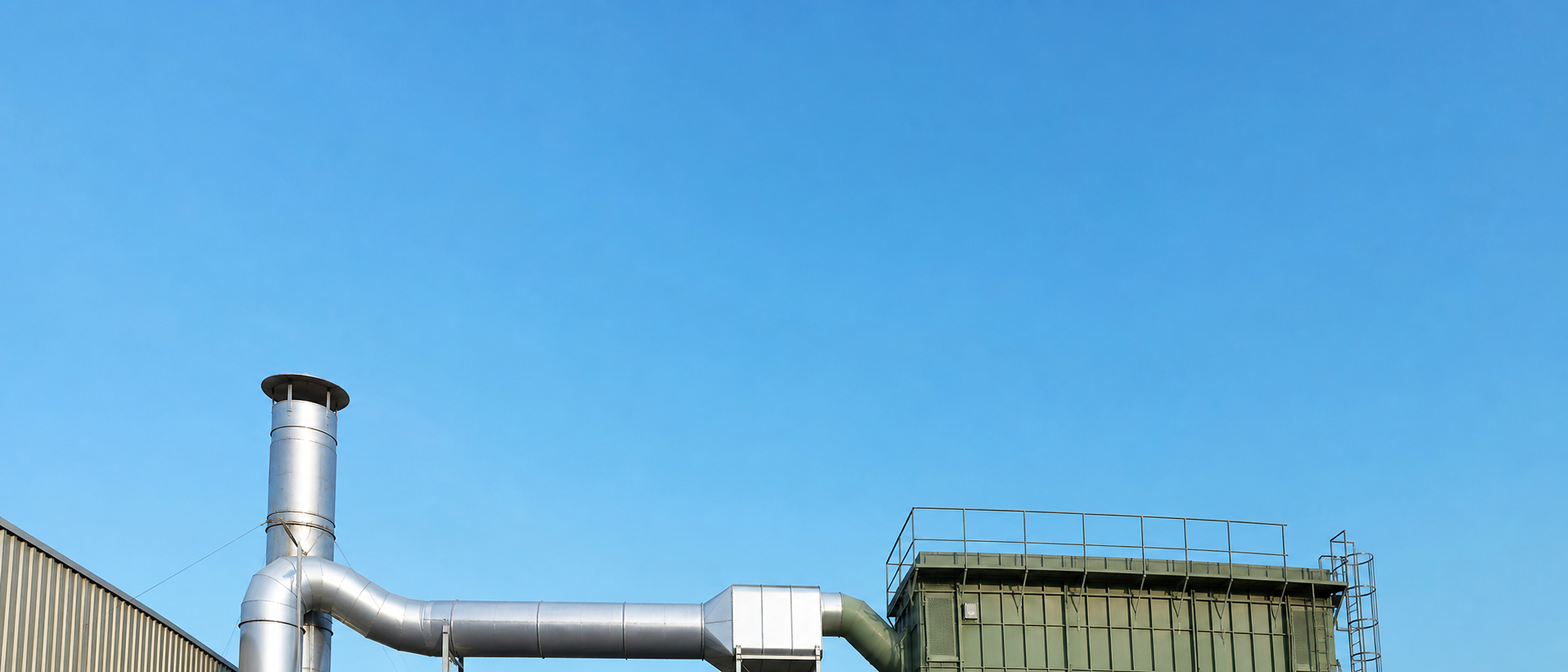 Rooftop dust collector and exhaust stack against a clear blue sky